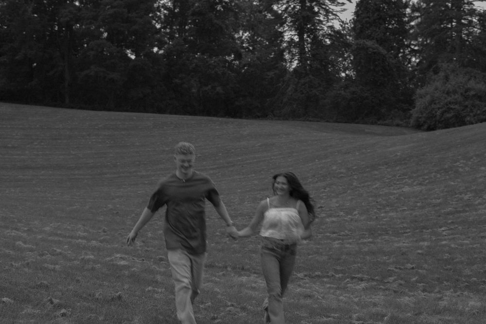 Man and woman running toward camera in field and holding hands
