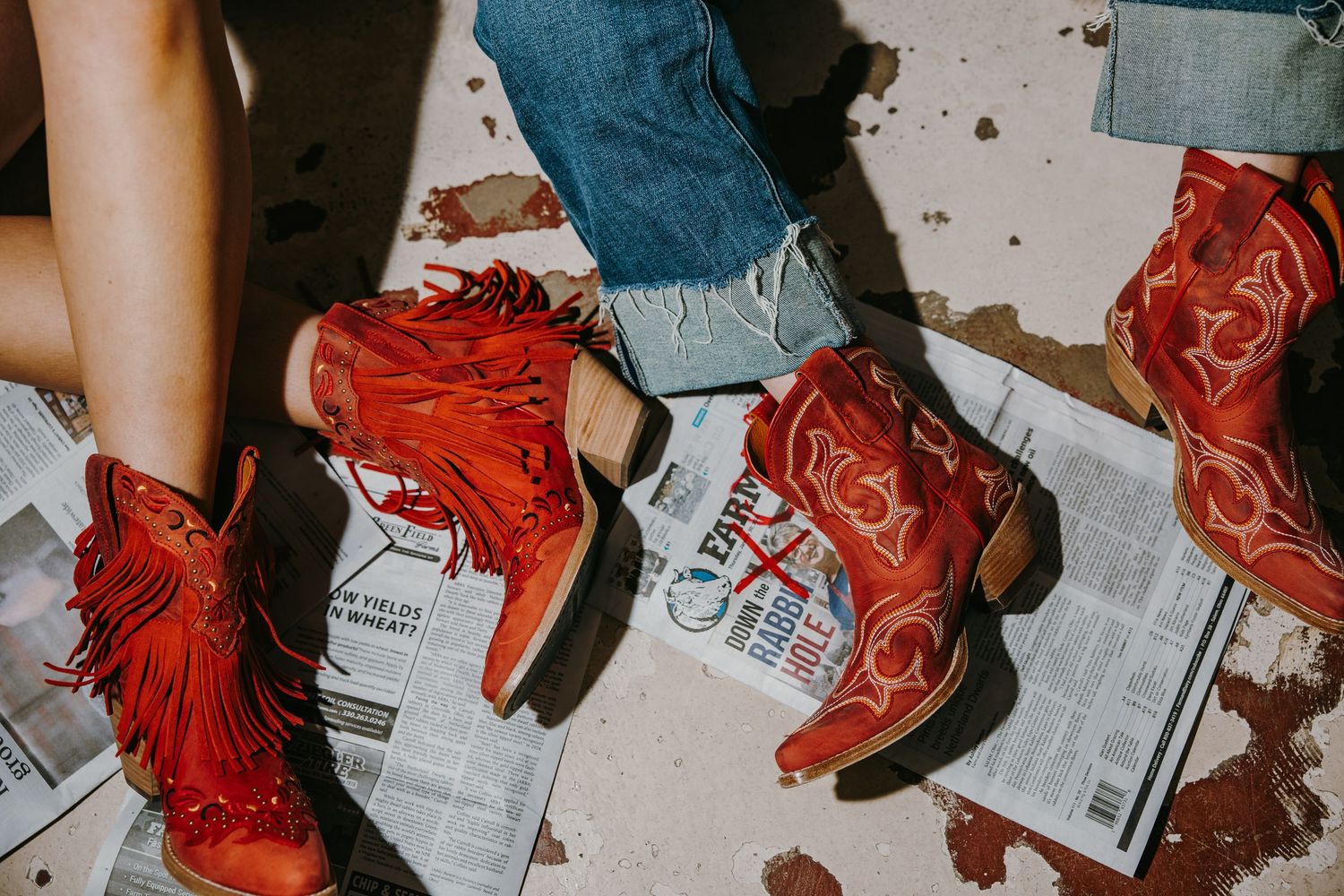 Red leather cowboy boots lined up in a row on a newspaper-covered surface, showing a western fashion display.