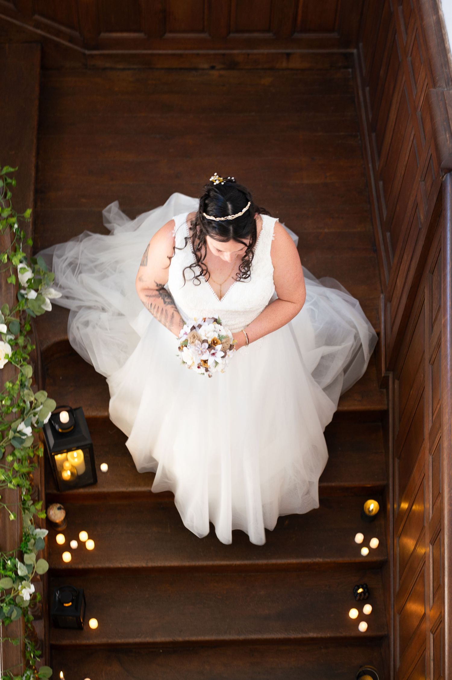 Top down view of a white tulle dress against rustic wooden stairs with string lights and greenery decorations.