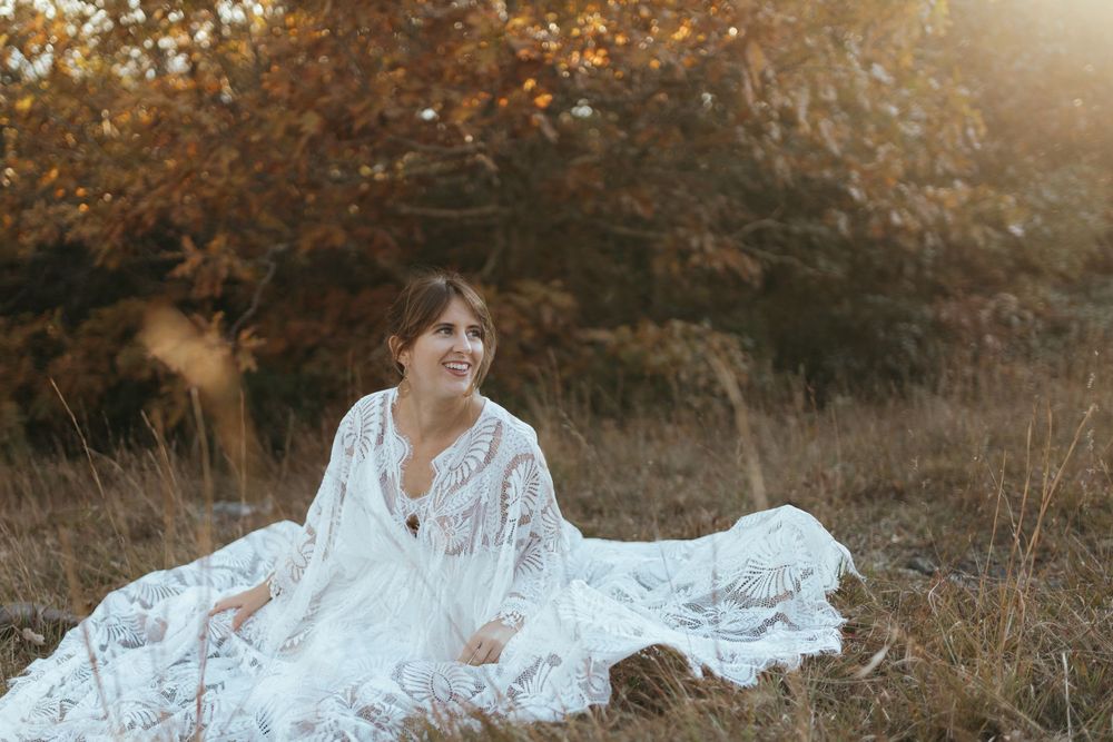 A person in a white lace dress poses in a sunlit autumn field during golden hour.