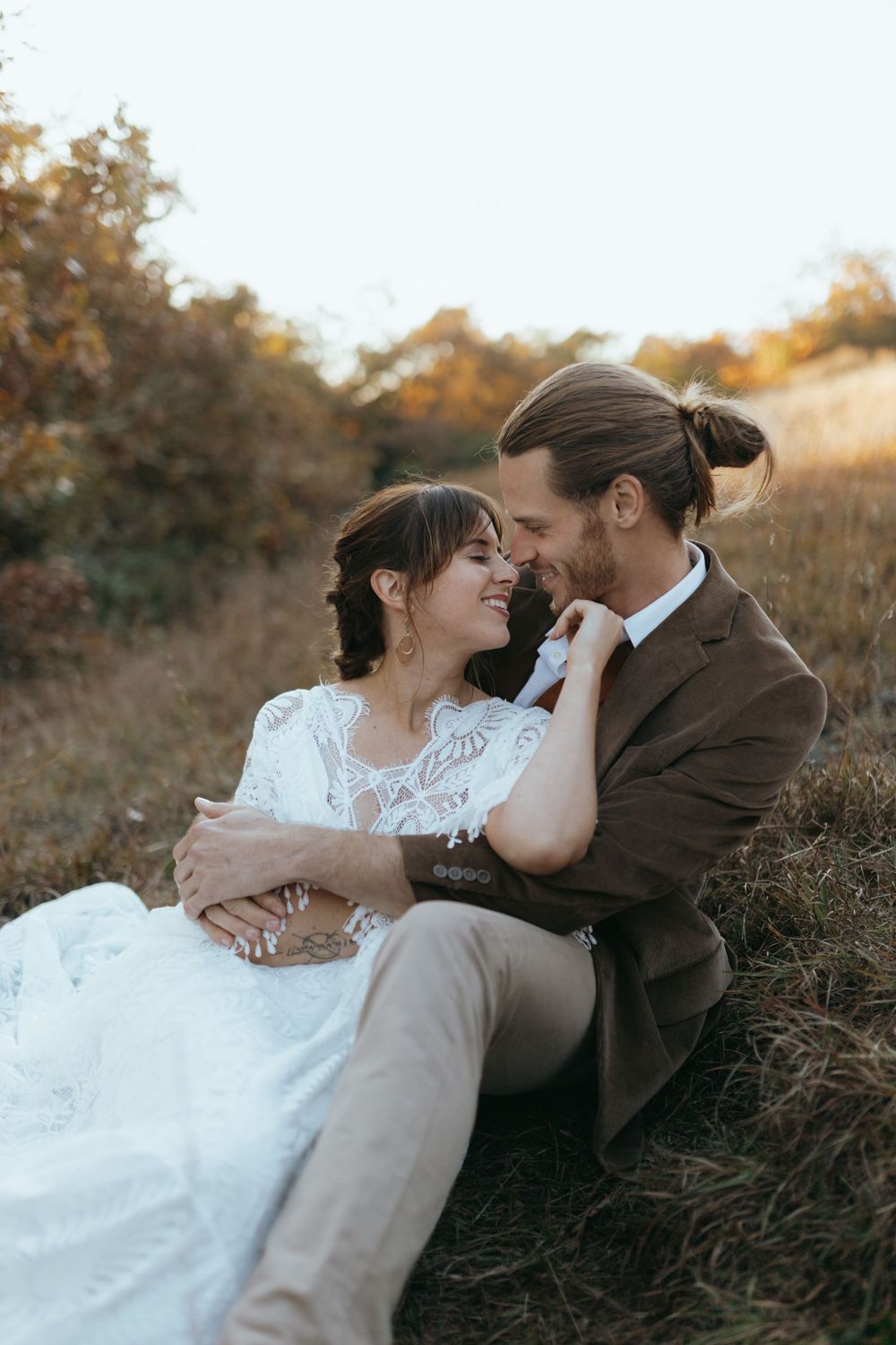 A tender moment between newlyweds sitting in autumn grass during golden hour.