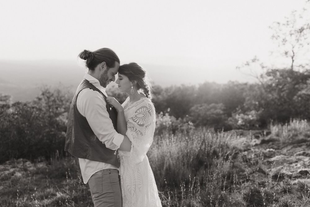 A romantic black and white photograph of a couple embracing on a hilltop during golden hour.
