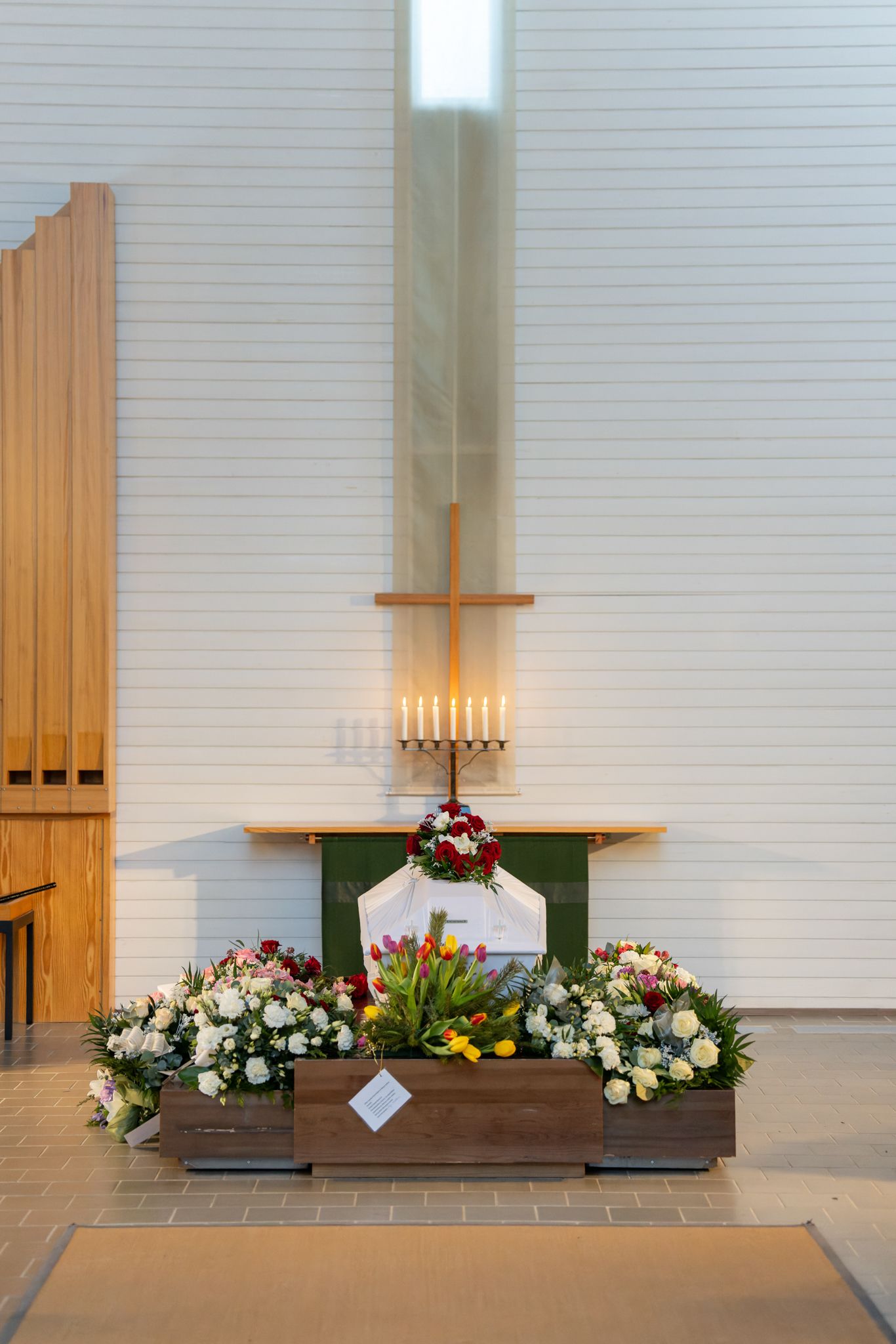 Church altar decorated with colorful floral arrangements and wooden organ pipes against a white wall.