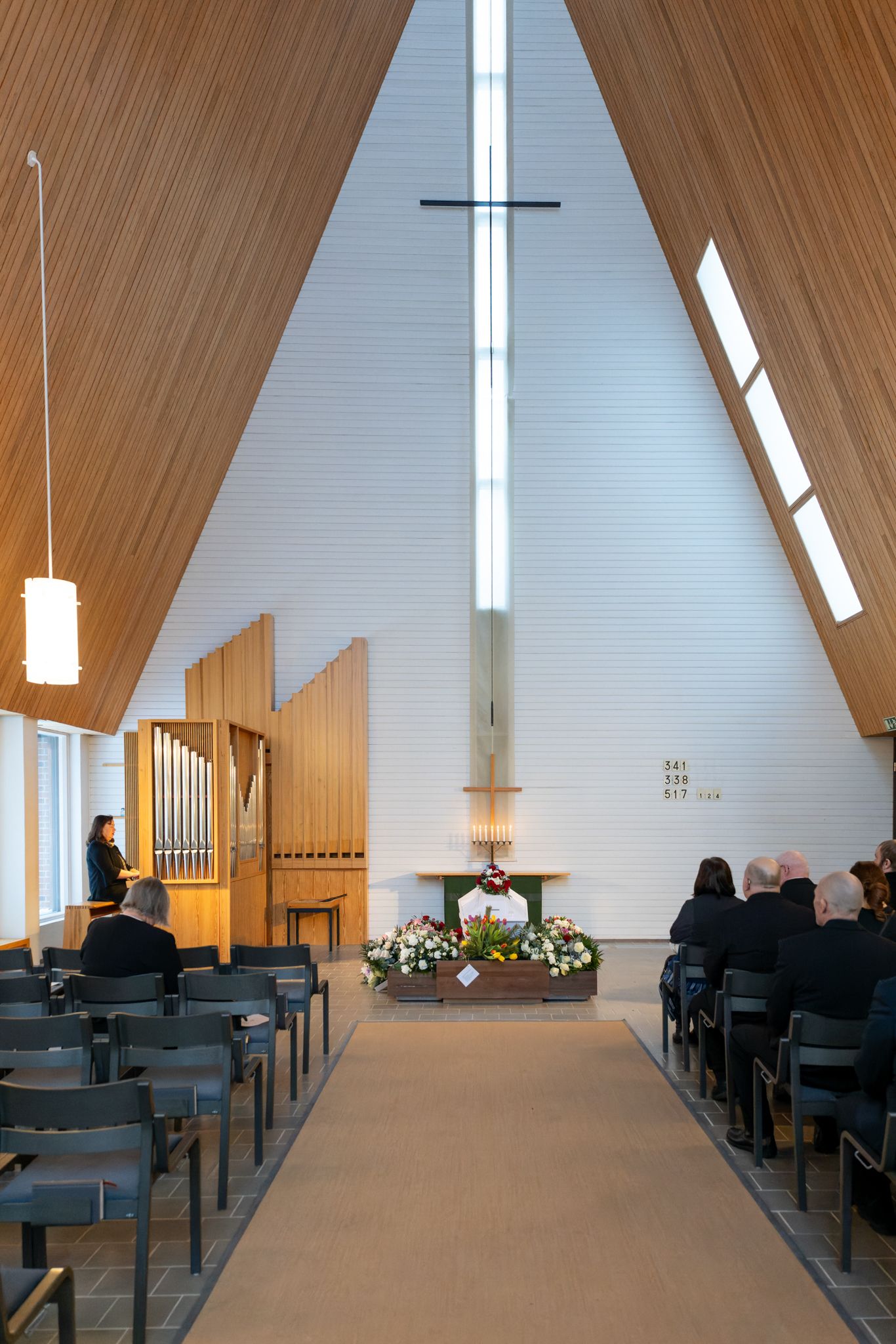 Modern church interior with wooden vaulted ceiling, white walls, and rows of gray chairs arranged in symmetrical formation.
