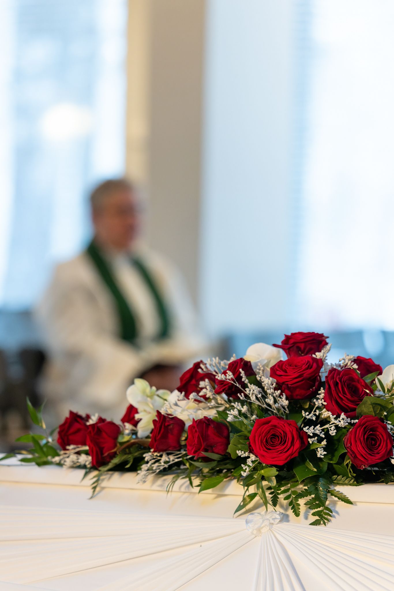 Red and white roses with greenery decorate a long white tablecloth at a formal event.