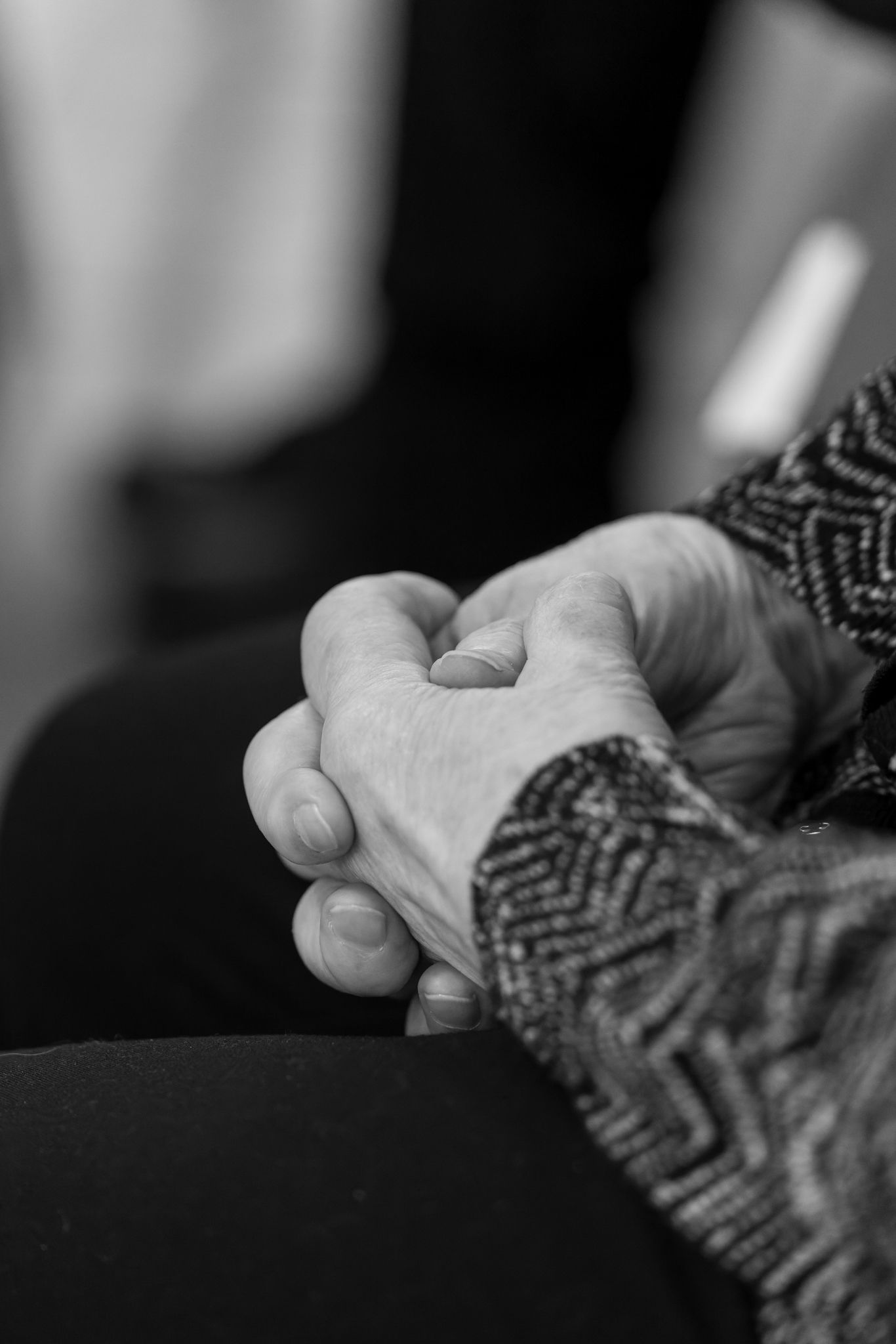 Black and white close-up of clasped hands with a textured sleeve showing comfort and connection.