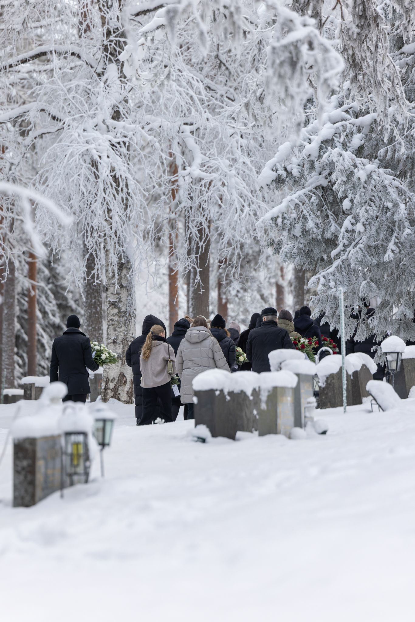 People walk through a snow-covered park with frost-covered trees creating a magical winter wonderland scene.