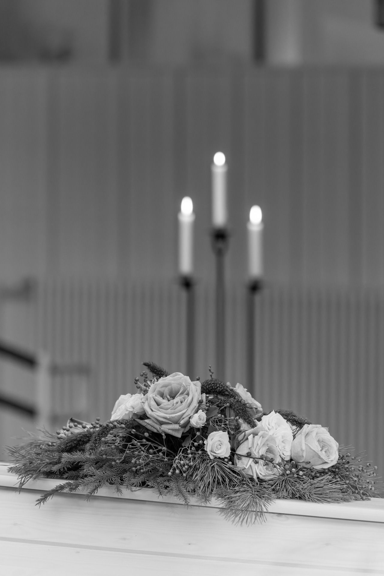 A black and white photograph of a long floral centerpiece with white roses and candles arranged on a surface.