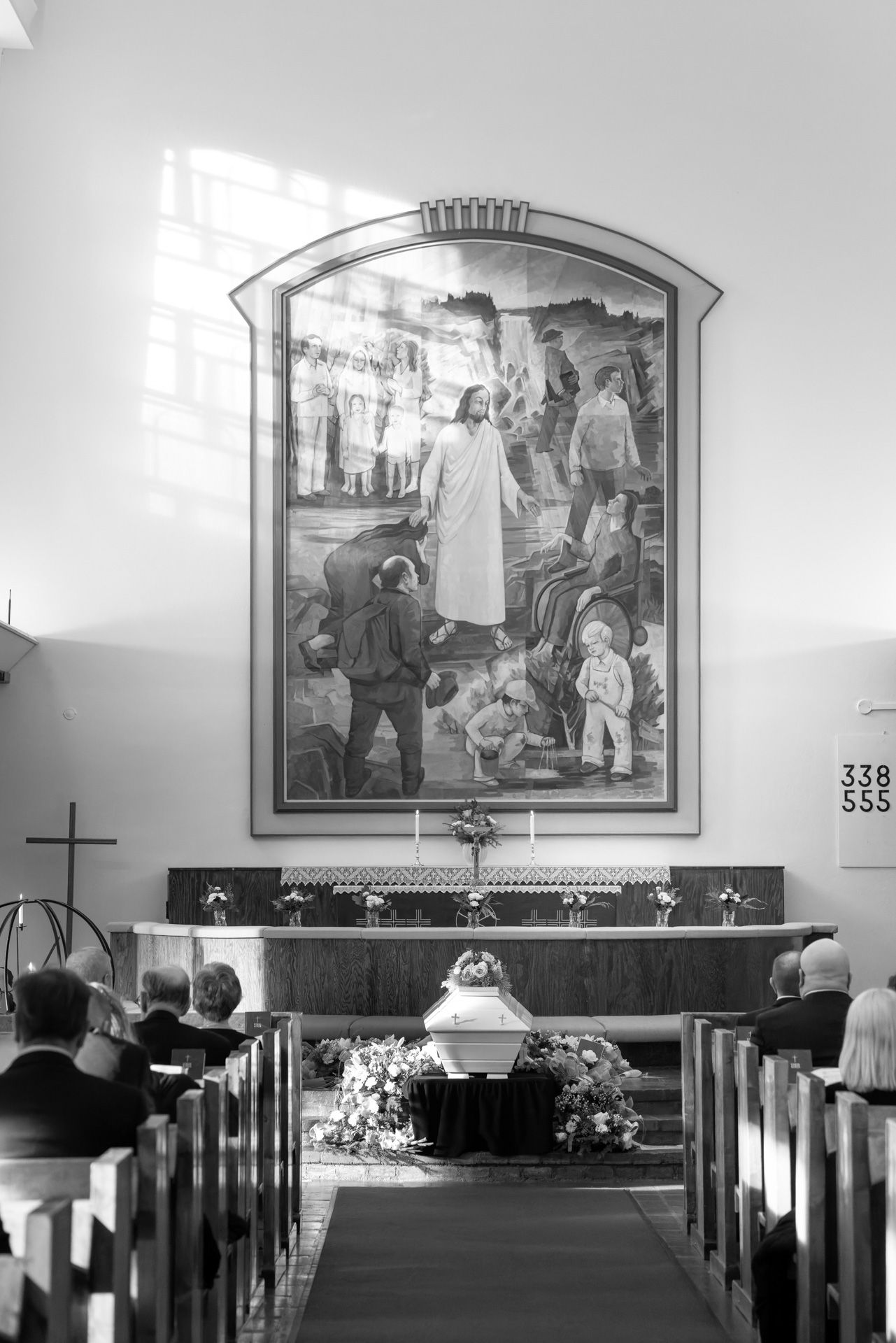 Black and white photograph showing church pews and religious murals mounted on walls in a traditional sanctuary interior.