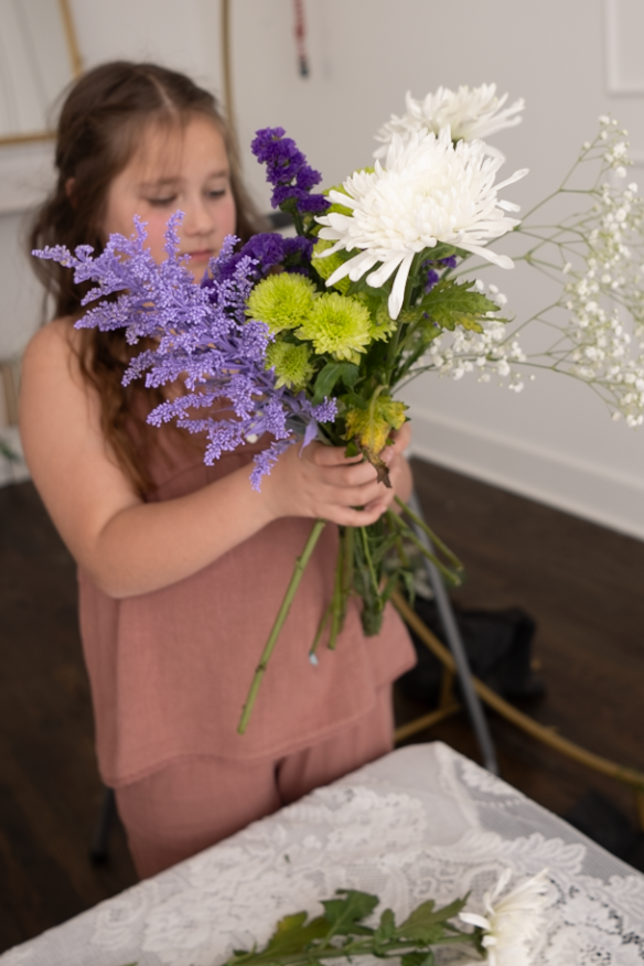 A sequence of images showing someone smelling a colorful bouquet of purple, white and yellow flowers against a white tablecloth.
