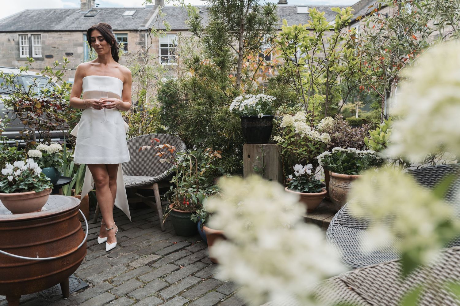 Person in white dress standing on urban rooftop garden patio surrounded by potted plants and flowers in Edinburgh.