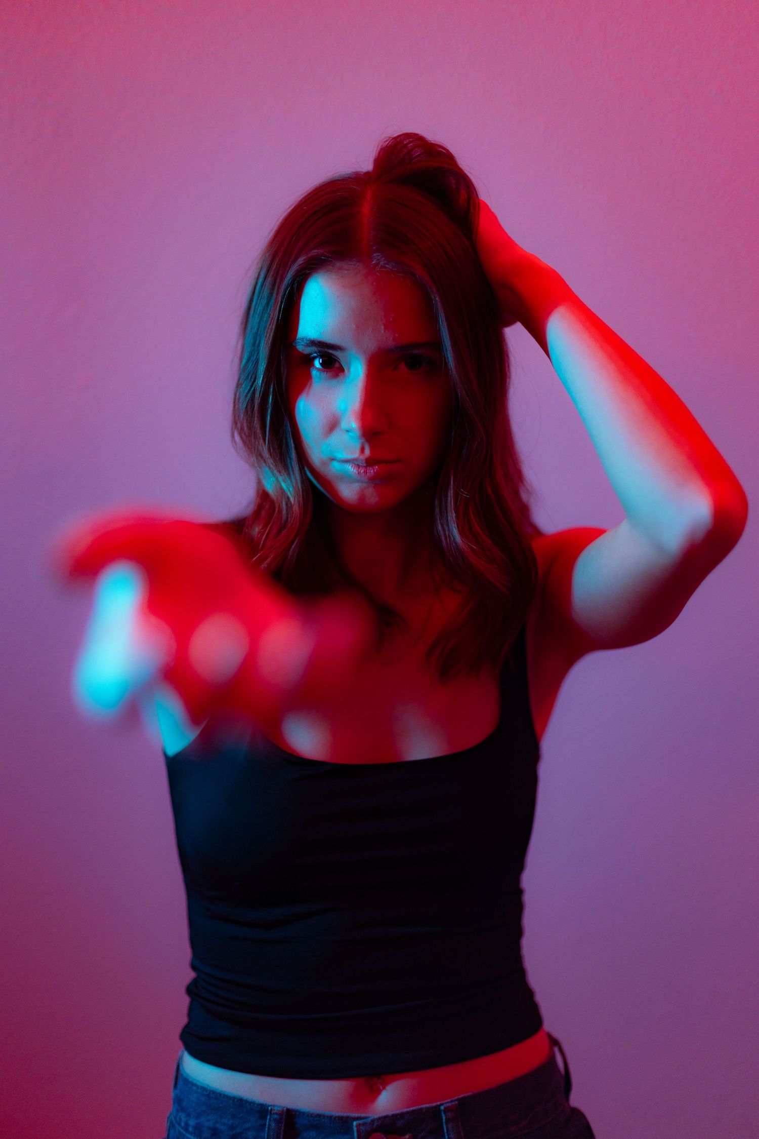 Artistic portrait with dramatic red and blue lighting effects illuminating figure in black tank top against gradient background.