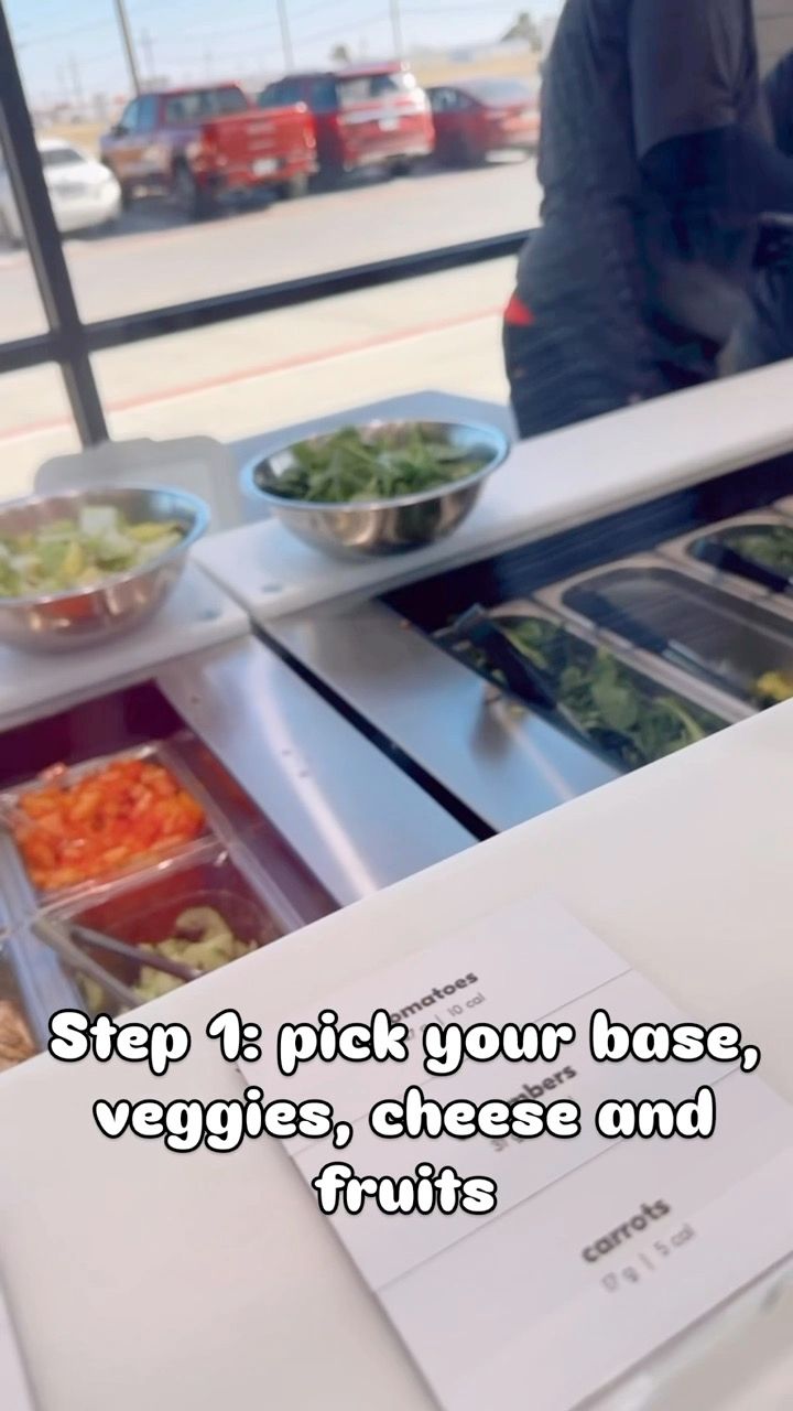 Food service counter showing various fresh ingredients including vegetables, cheese and fruits for customizable meal assembly.