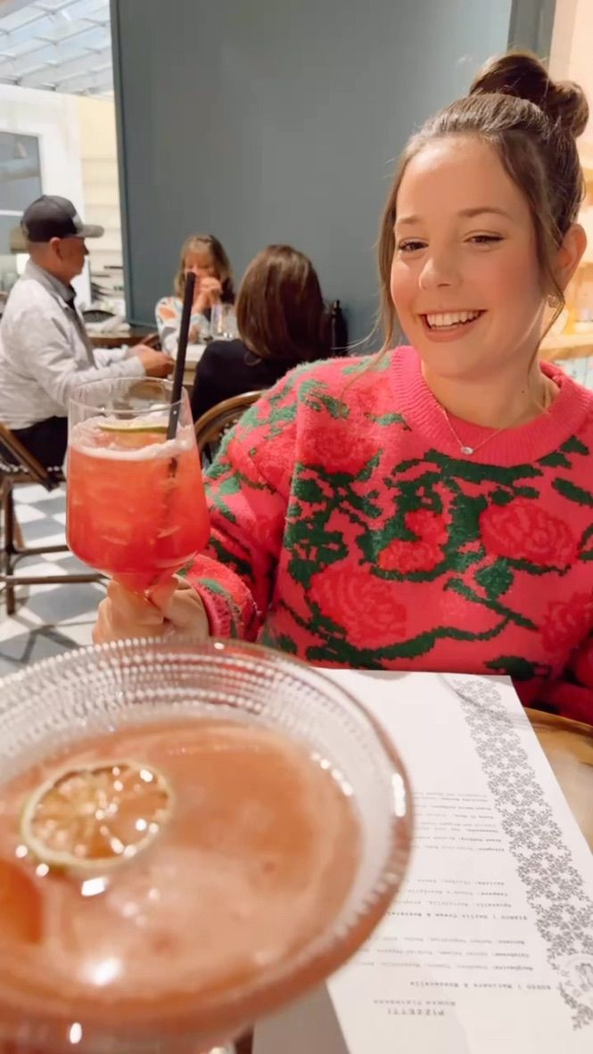A diner enjoying cocktails at a restaurant while wearing a festive red and green floral sweater.