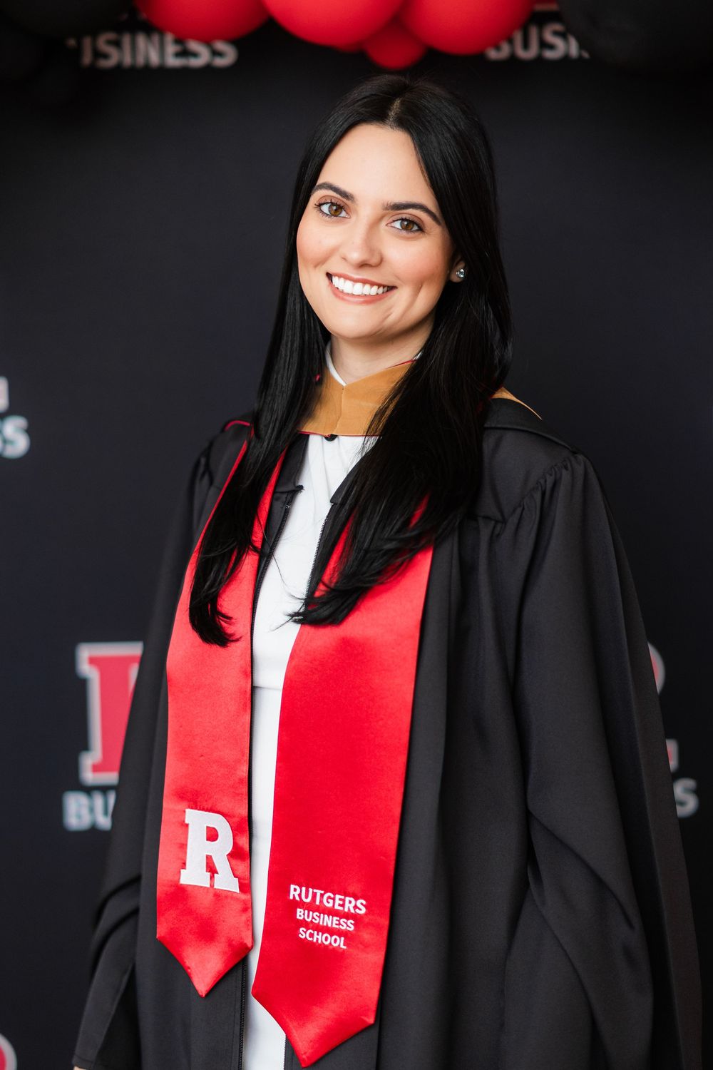 Graduate wearing black graduation gown and red Rutgers stole poses against dark background.