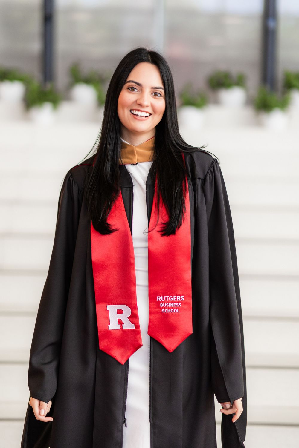Graduate wearing black gown and red Rutgers stole poses for series of graduation photos outdoors.