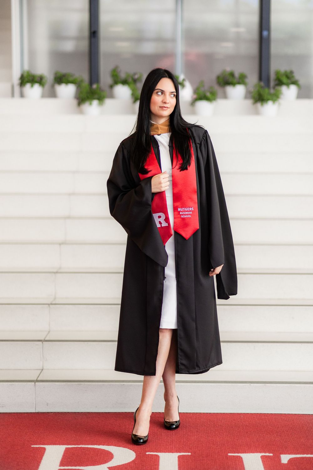 Graduate posing on stone steps in black graduation gown and red stole at Rutgers University.