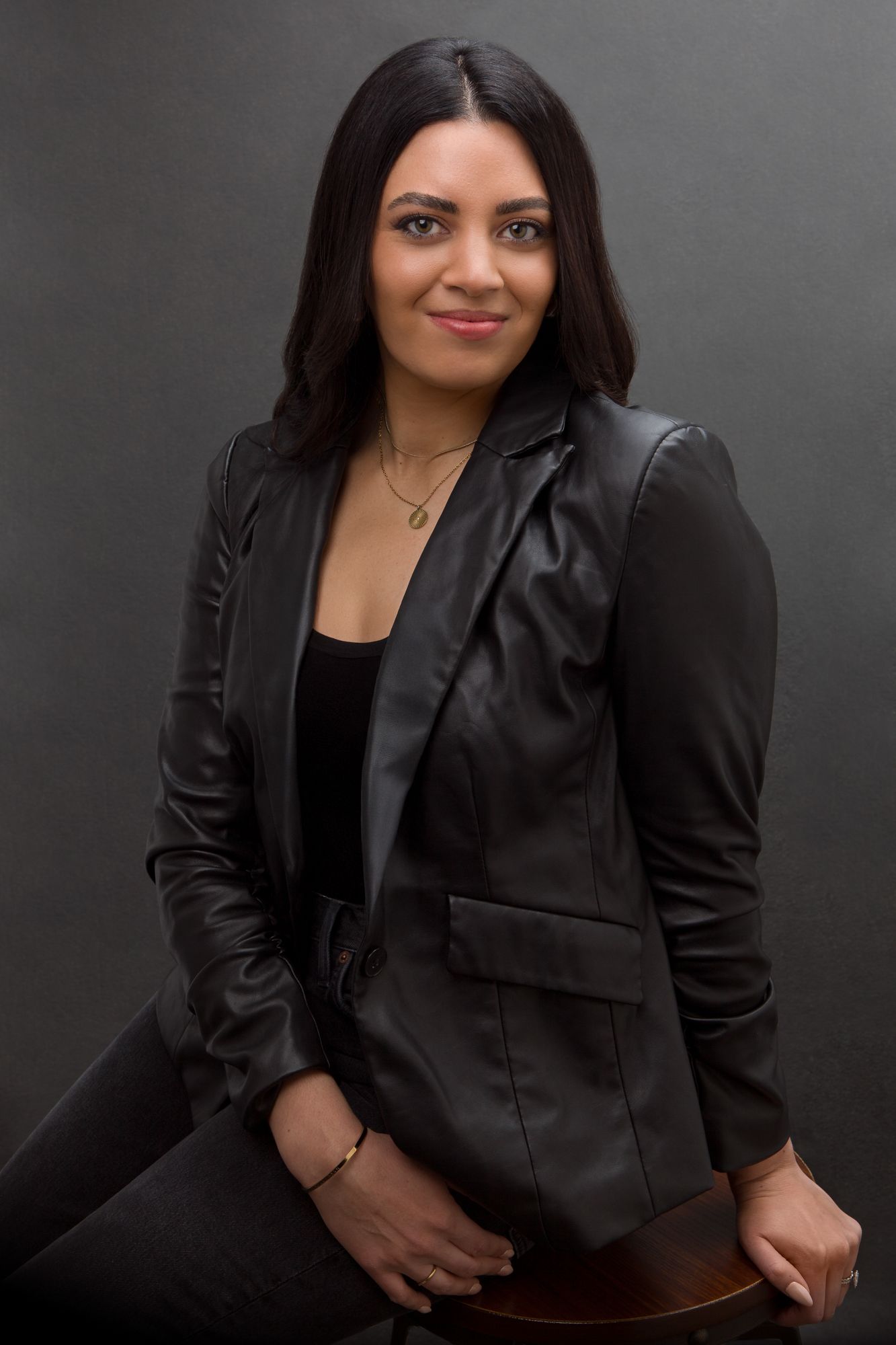 Professional portrait of someone in a black blazer and top against a dark gray background.