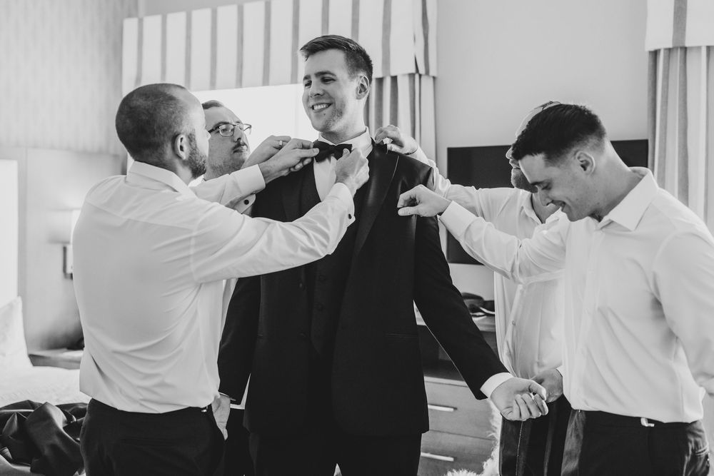 Groomsmen in white shirts and black suits perform synchronized dance moves at a wedding reception.