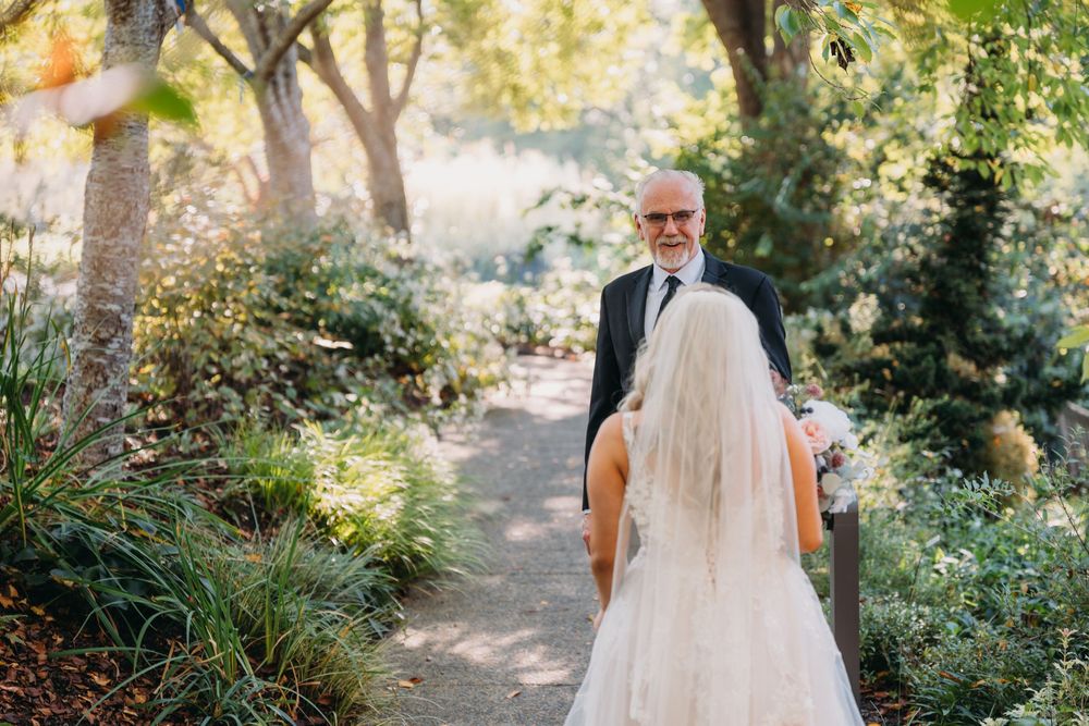 A touching first look moment between father and bride in a sunlit garden pathway.