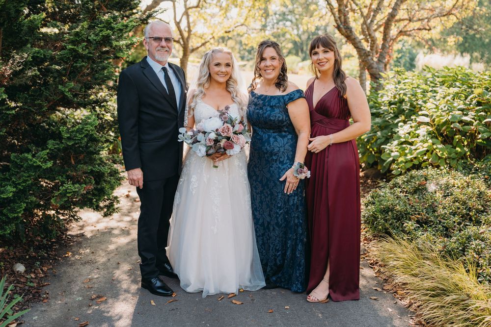 Wedding party poses together on a garden path surrounded by lush greenery and trees.