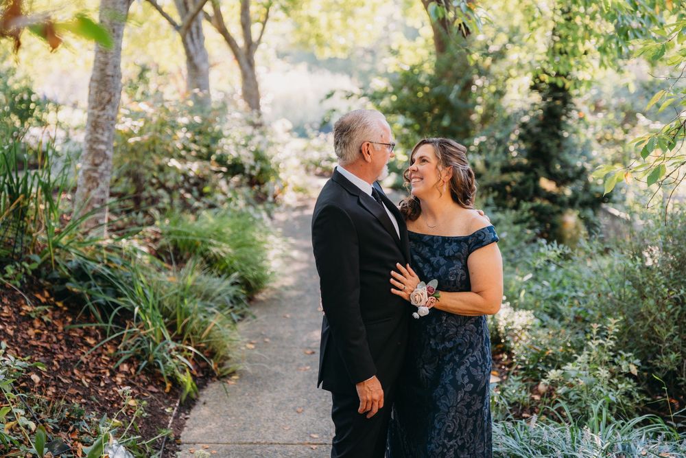 A couple shares a tender dance moment in a sunlit garden pathway surrounded by trees.