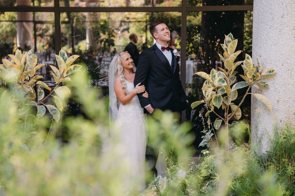 Wedding ceremony moment captured through blooming garden foliage with white columns.