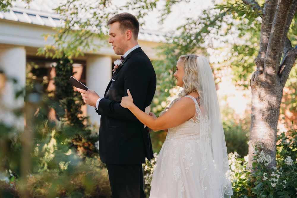 A couple shares a private moment reading vows in a lush garden setting.
