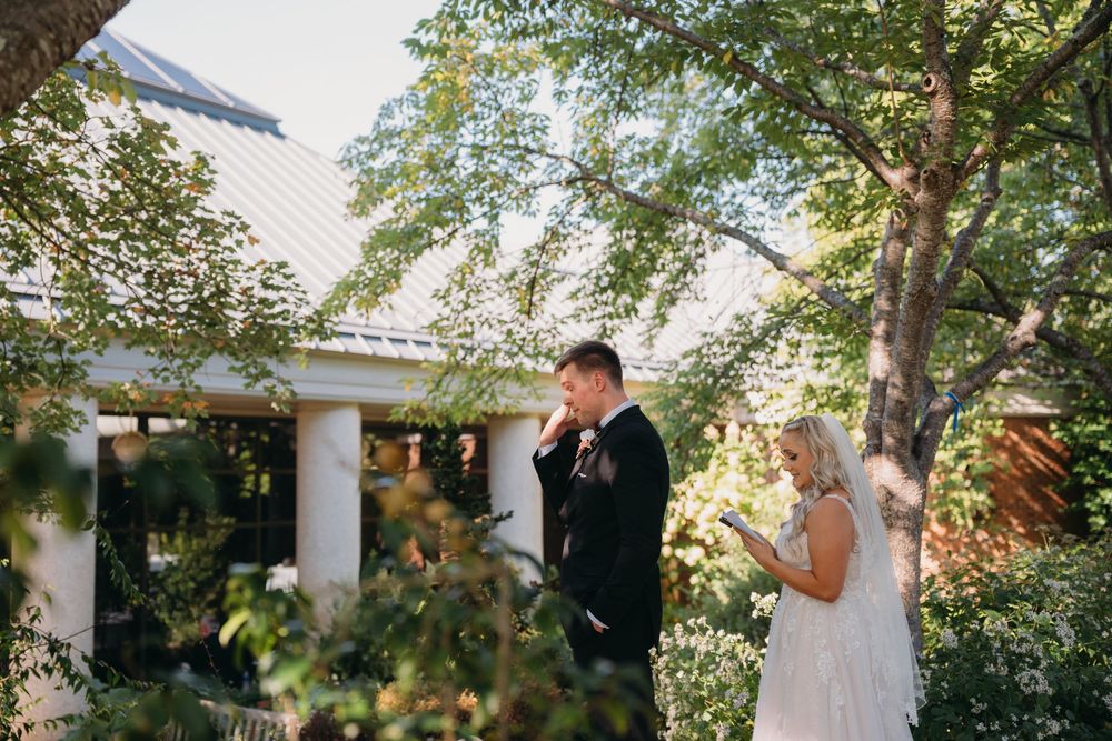 An emotional wedding ceremony moment in a garden with white pillars and greenery.