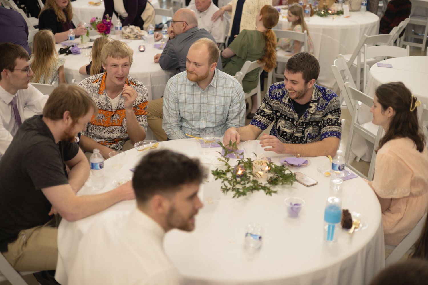 Wedding reception guests seated at an elegantly decorated round table with floral centerpiece.