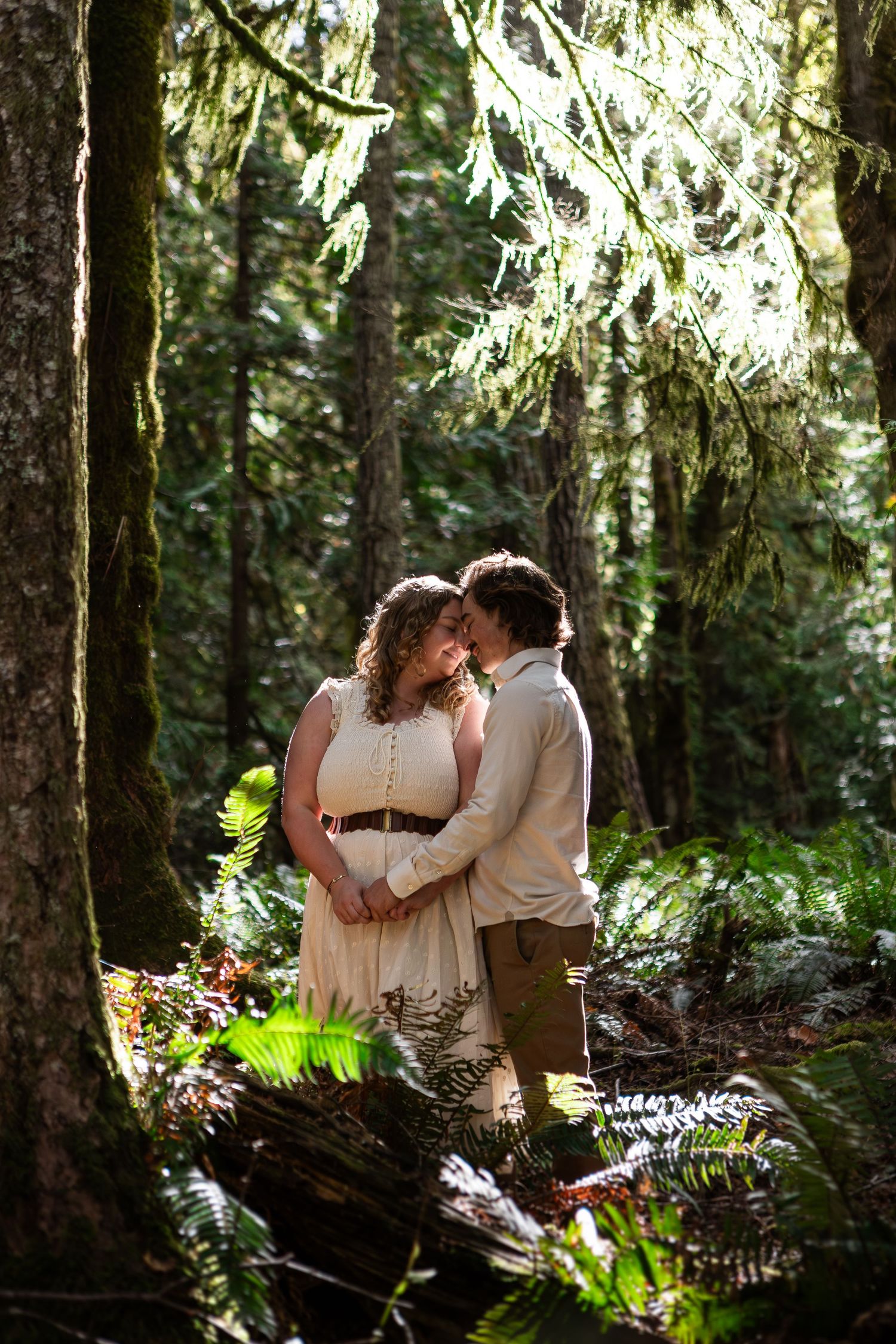 Romantic forest engagement photos with couple among moss-covered trees and ferns.