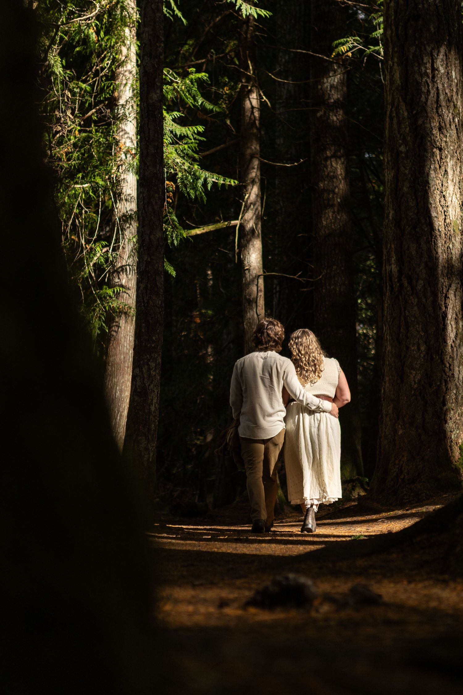 Couple walking hand in hand through a sunlit forest path.