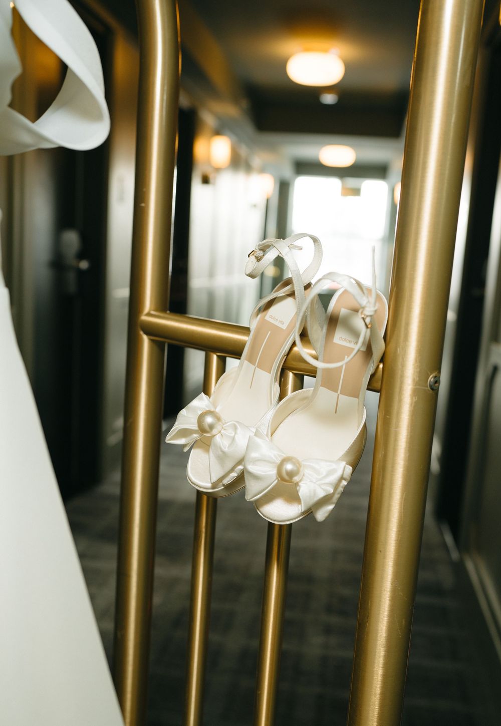 White pearl-adorned bridal shoes displayed on golden metal rails in a hallway.
