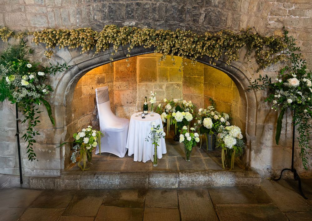 Elegant stone archway decorated with white roses and greenery creates a romantic wedding setting in grand hall of Allington Castle in Kent