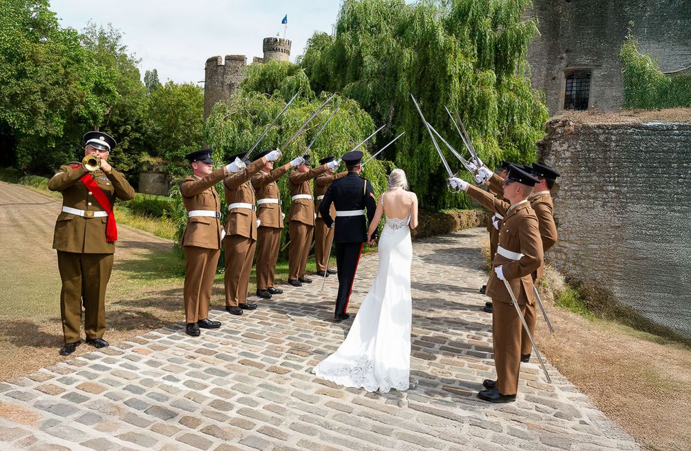 Military honor guard forms a ceremonial arch with swords as a bride in white gown walks through at Allington Castle in Kent.