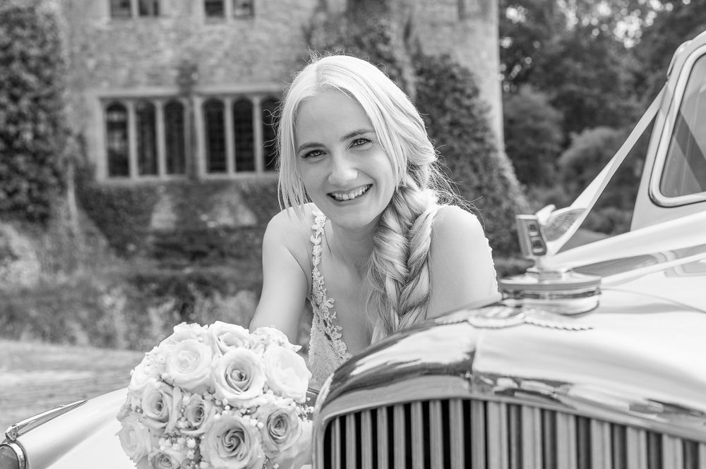 Black and white wedding image showing bride leaning on vintage car and floral details | Allington Castle in Kent