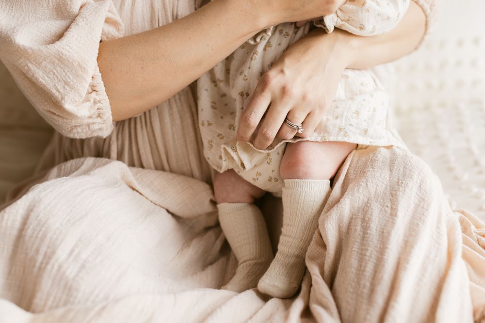 A close up view of a wedding ring of a mother holding her newborn girl wearing a cream floral dress for newborn photos in Essex County, MA