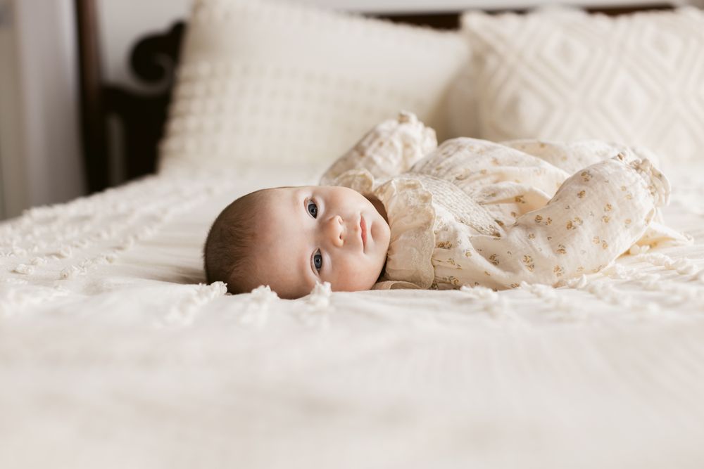Dover, Southern NH and Maine, Lenox, North Shore, Cohasset newborn photographer. Newborn baby girl wearing a light floral dress lays on bed