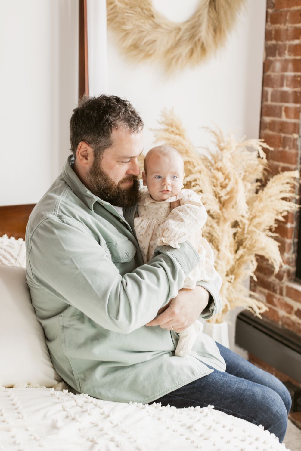 A father with a beard wears a mint colored shirt and dark blue jeans holding his newborn girl at the Little Loft in North Andover, MA