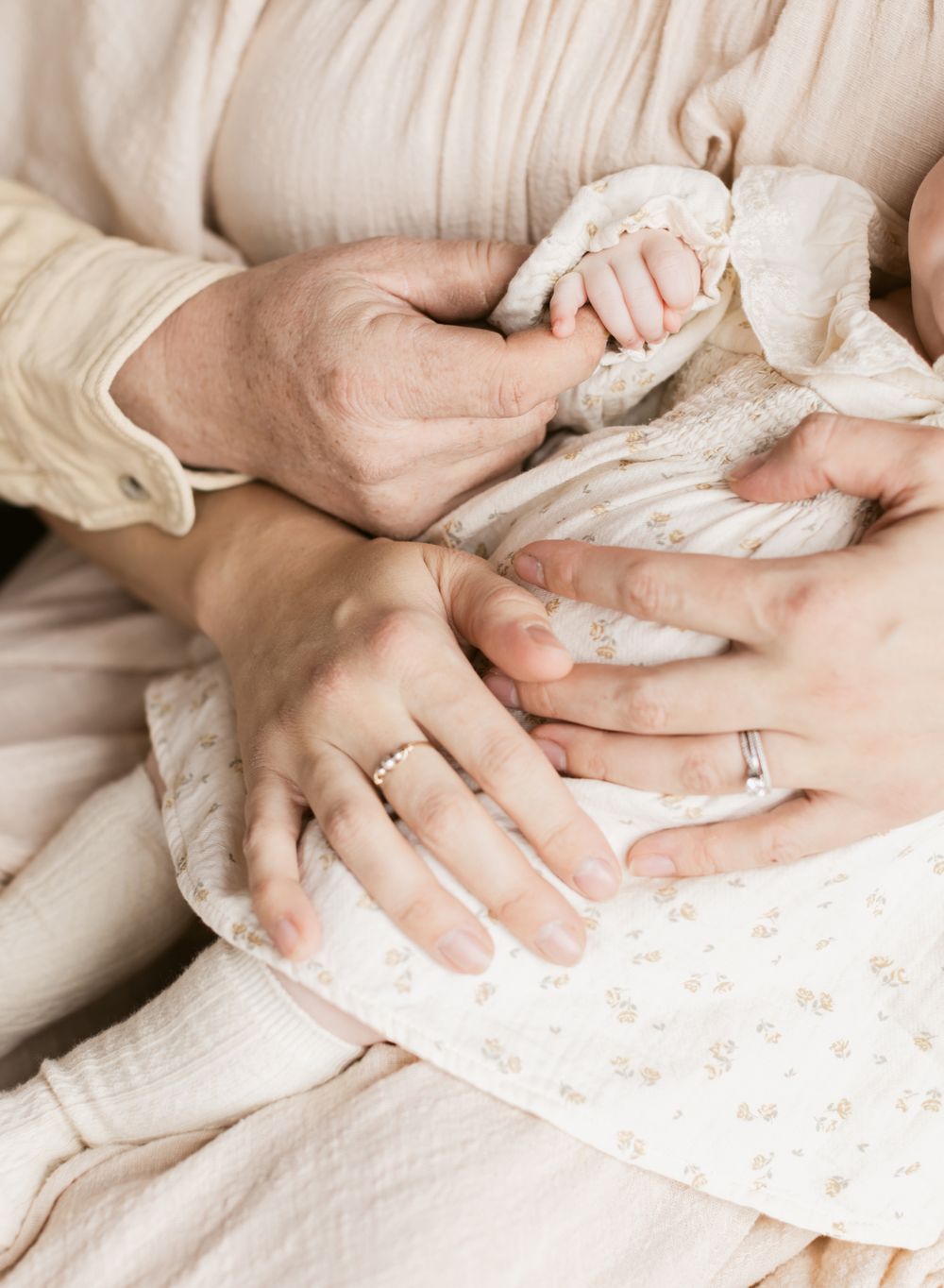 A close up shot of parents hands holding their newborn girl wearing a cream colored floral dress at the Little Loft in North Andover, MA.