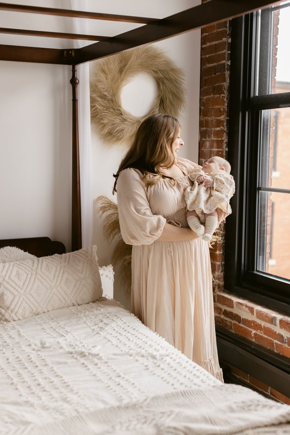 A mother with brown hair wearing a cream dress holds her newborn gazing at her at the Little Loft in North Andover, MA for newborn photos.