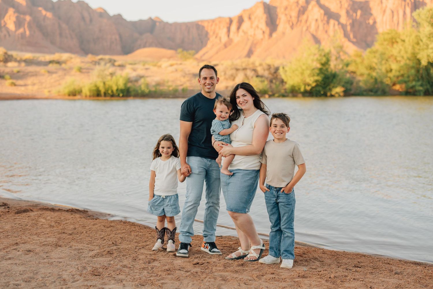 Family in coordinated blue and white outfits sharing candid moments during golden hour beach photoshoot.
