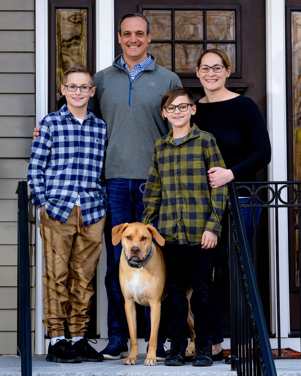 Family and their brown dog posing together on their front porch steps.