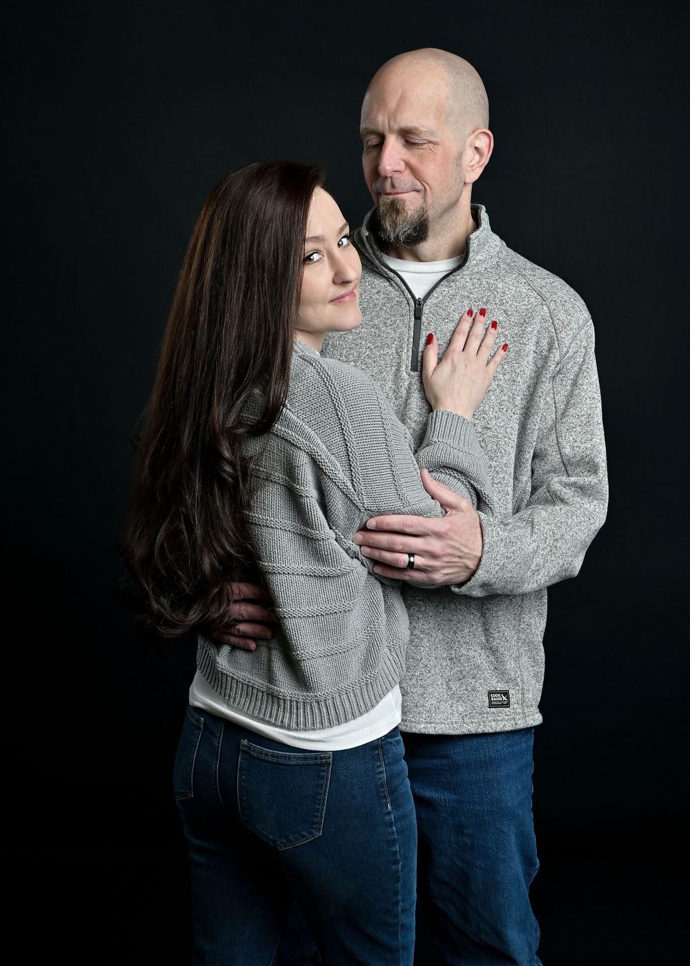 Intimate portrait of a couple in matching gray sweaters against a dark background.