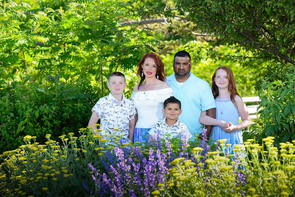 Happy family of five posing together in a garden with colorful summer flowers.