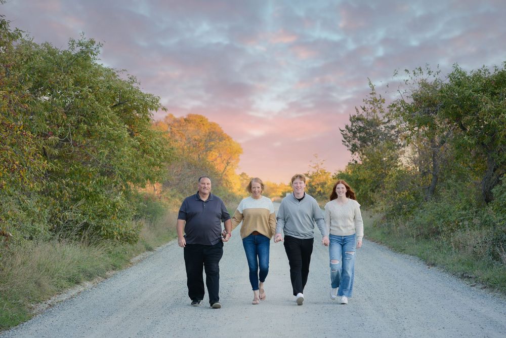 Family of four walking together on a dirt road during sunset.