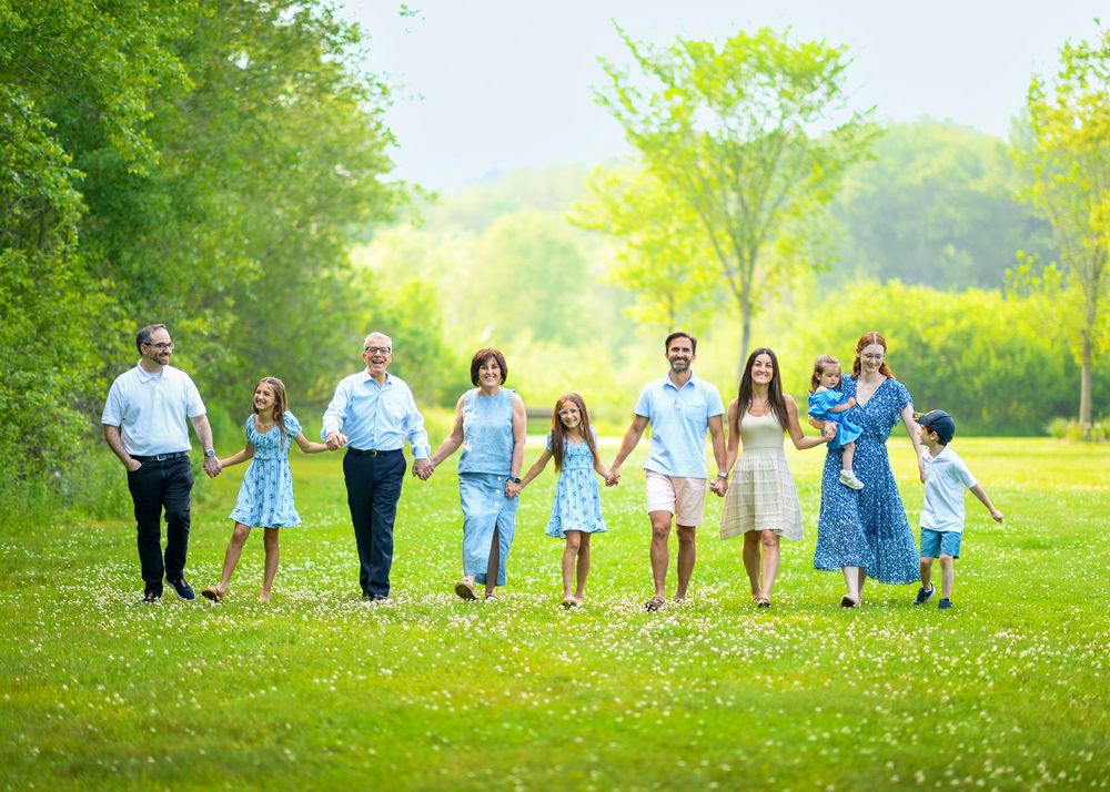 Group holding hands in a line across a sunny meadow with green grass and trees.