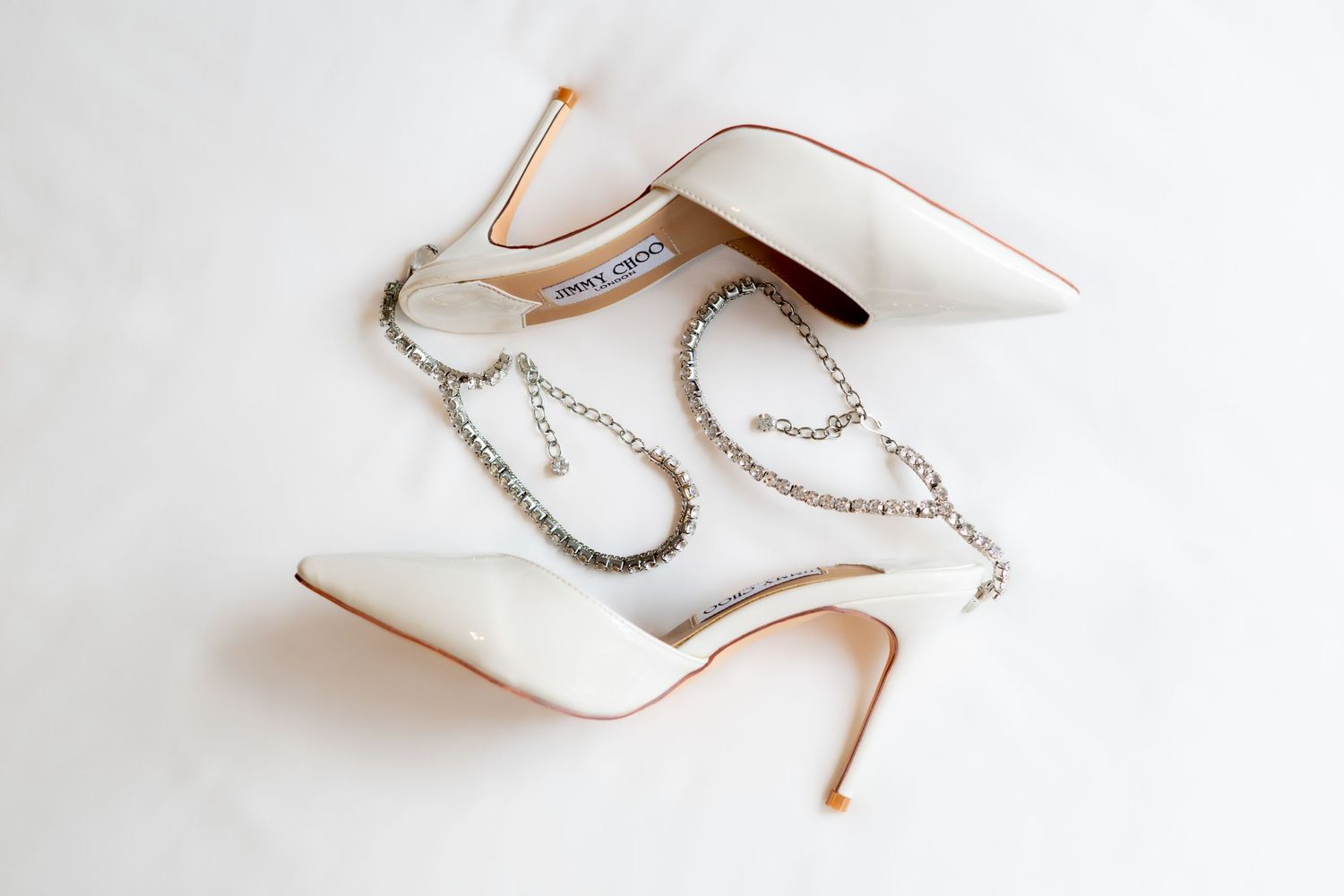 Elegant white stiletto heels with pearl chain accessories displayed on a light background.