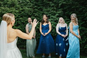 A bride stands with her bridesmaids wearing different shades of blue and green dresses in an outdoor garden setting.