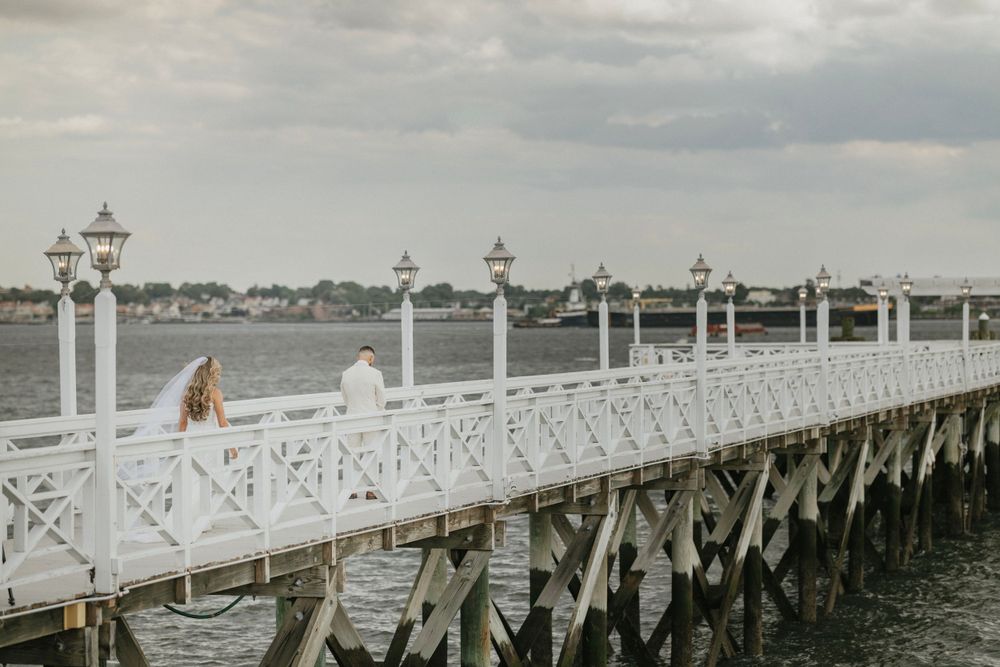 A white coastal pier with decorative lamp posts stretches over calm waters on a cloudy day.